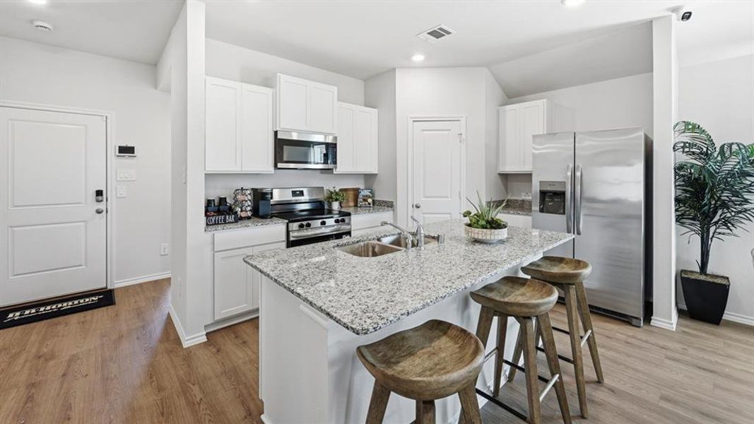 Modern kitchen featuring white cabinetry, stainless steel appliances, a large island with a dual-basin sink, and light-colored countertops