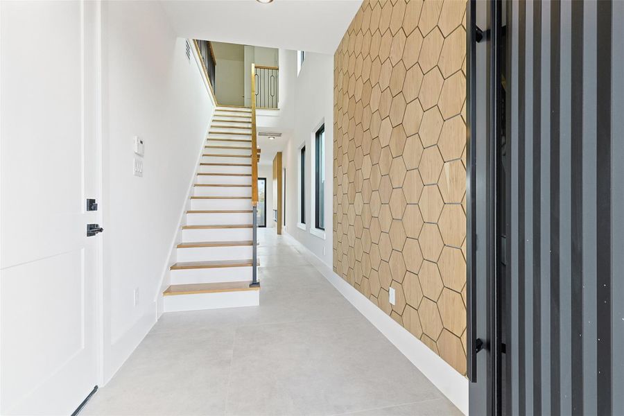 The entryway showcases a floor-to-ceiling hexagonal wood accent wall and a staircase with natural wood treads and black iron railings.