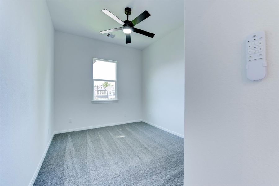 Secondary bedroom with plush carpet, a ceiling fan with integrated light kit, and a large window bringing in natural light. Clean, neutral finishes create a bright and comfortable space.