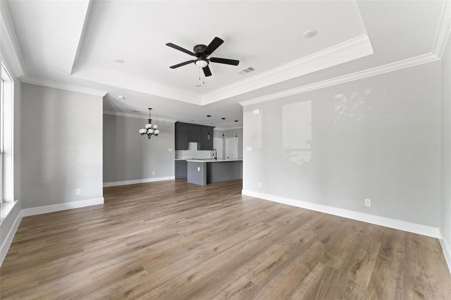 Unfurnished living room with a tray ceiling, a chandelier, light wood-style floors, crown molding, and a ceiling fan
