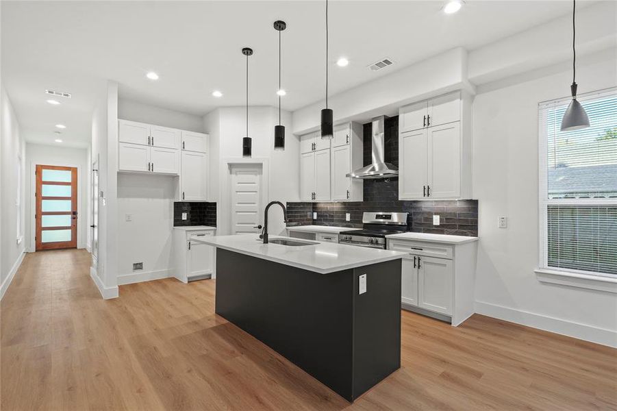 Kitchen with white cabinetry, stainless steel range oven, sink, and wall chimney range hood