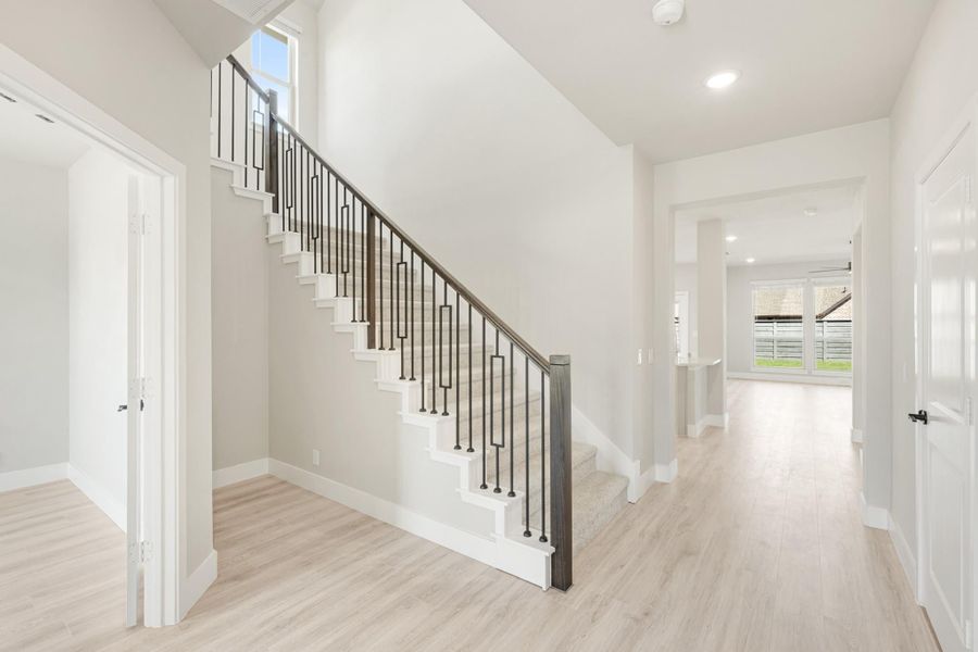 Bright entryway with staircase featuring black metal balusters and light wood floors leading to hallway