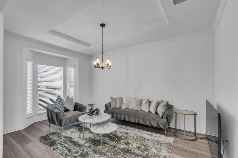 Living room featuring a raised ceiling, hardwood / wood-style flooring, crown molding, and a chandelier