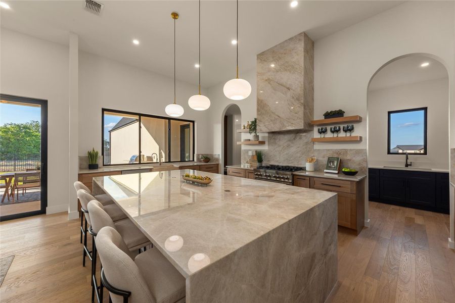 Kitchen with light stone counters, arched walkways, a breakfast bar, and light wood-style flooring
