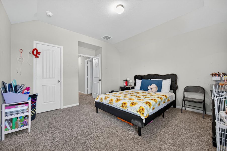 This bedroom features a cozy layout with neutral walls and carpeted flooring. It has a bed with a cheerful sunflower-themed comforter, and there's ample space for storage with shelves and a closet. The room is well-lit, creating a welcoming atmosphere.