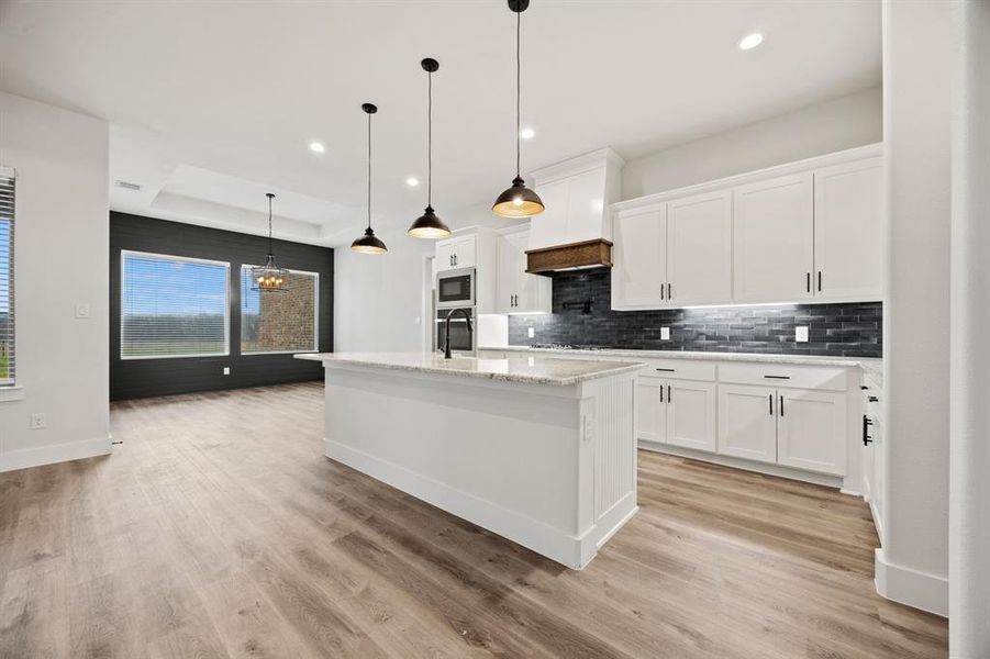 Kitchen featuring built in microwave, pendant lighting, and white cabinetry