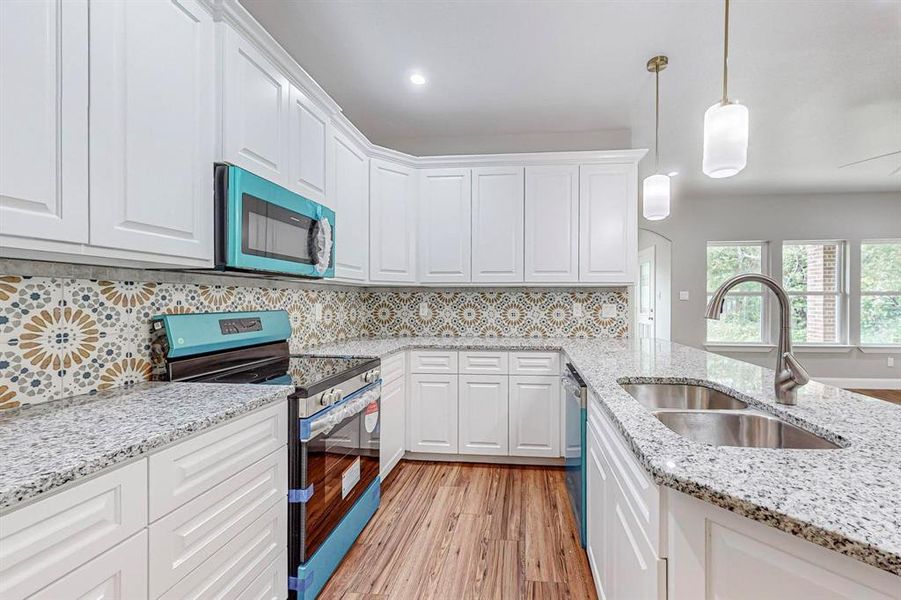 Kitchen featuring sink, tasteful backsplash, white cabinetry, stainless steel appliances, and light hardwood / wood-style flooring