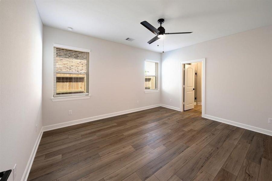 Experience serenity in the primary bedroom, where vinyl plank flooring invites barefoot comfort and a ceiling fan gently stirs the air. Ample windows allow natural light to cascade into the space, enhancing its welcoming ambiance