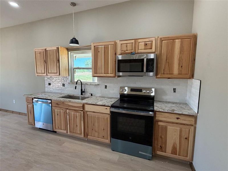 Modern kitchen featuring light wood cabinetry, stone countertops, and stainless steel appliances