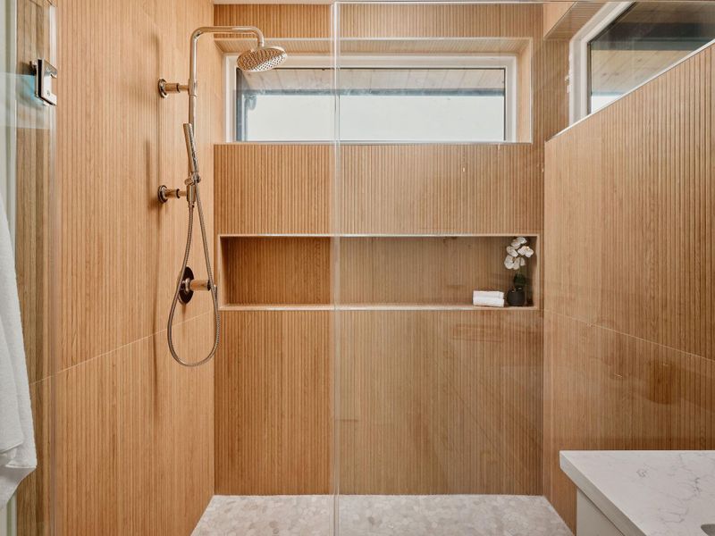 Walk-in shower with full-height wood-finish fluted wall tiling, integrated niche shelving, and a rain shower head with an additional handheld sprayer