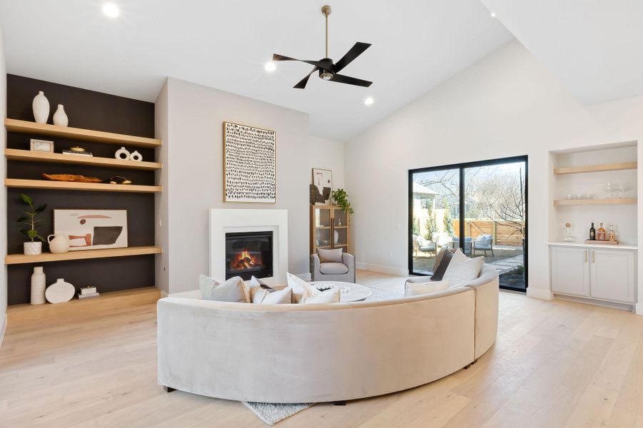 Living area featuring a glass covered fireplace, high vaulted ceiling, light wood-type flooring, and built in features