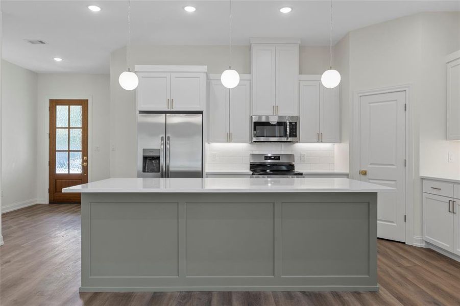 Kitchen featuring backsplash, stainless steel appliances, white cabinetry, pendant lighting, and dark wood-type flooring Kitchen featuring backsplash, stainless steel appliances, white cabinetry, pendant lighting, and dark wood-type flooring