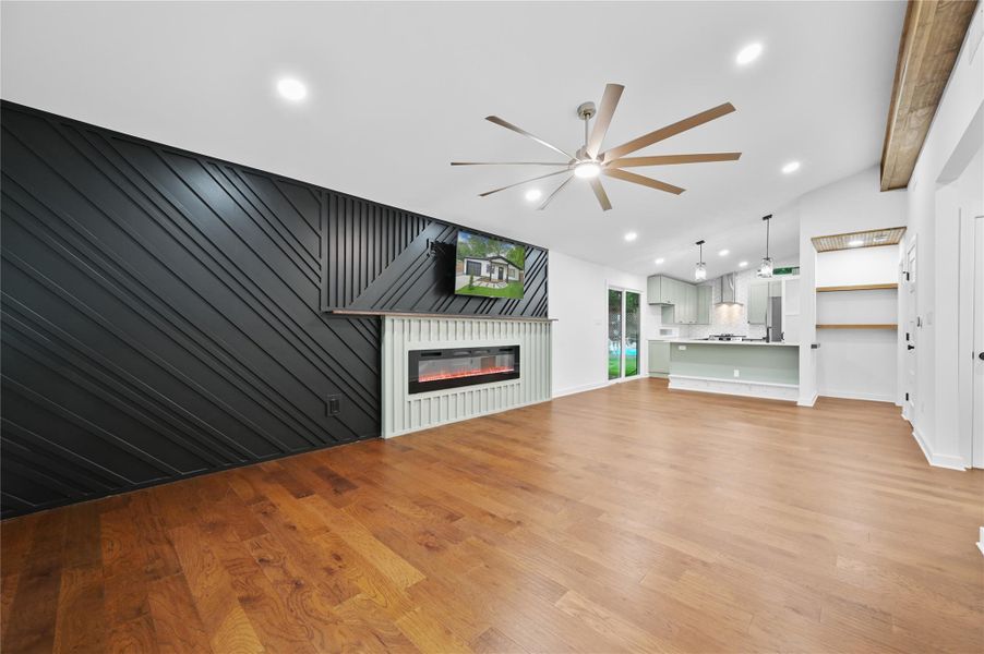 Unfurnished living room featuring ceiling fan, light wood-style floors, lofted ceiling, a glass covered fireplace, and recessed lighting