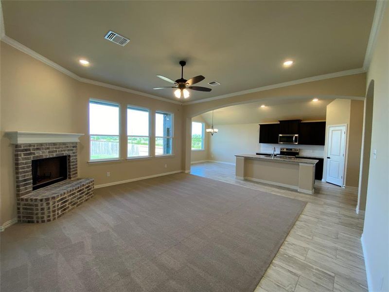 Unfurnished living room featuring crown molding, ceiling fan, a fireplace, and light colored carpet