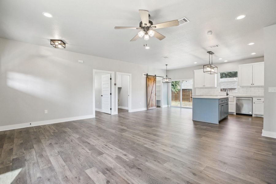 Unfurnished living room with a barn door, recessed lighting, a ceiling fan, and dark wood-type flooring