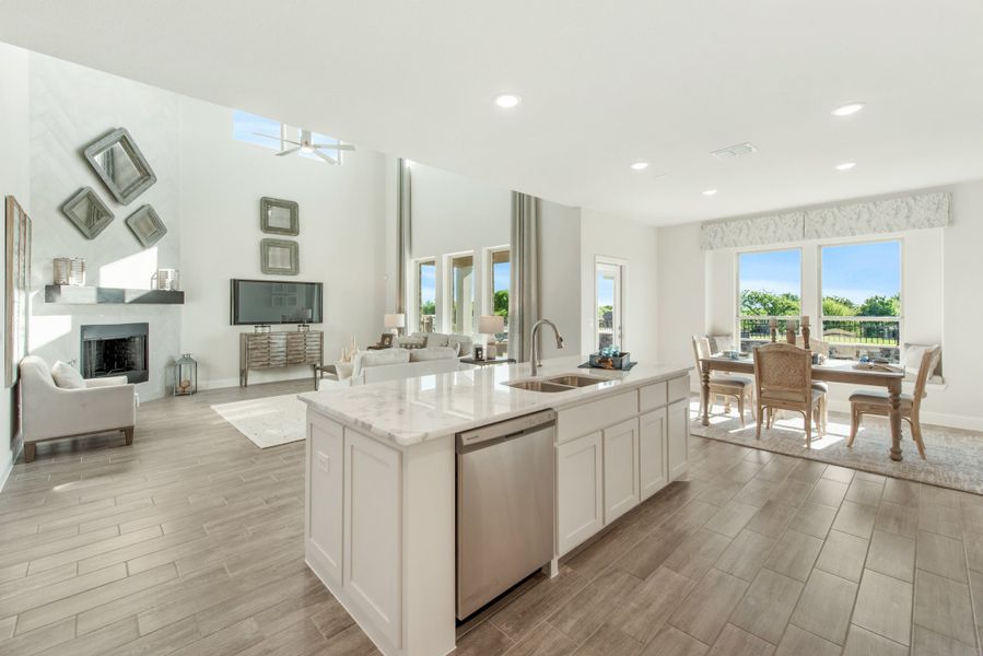 Open-concept kitchen with white island, quartz countertops, and views into living and dining areas with fireplace and wood-look floors
