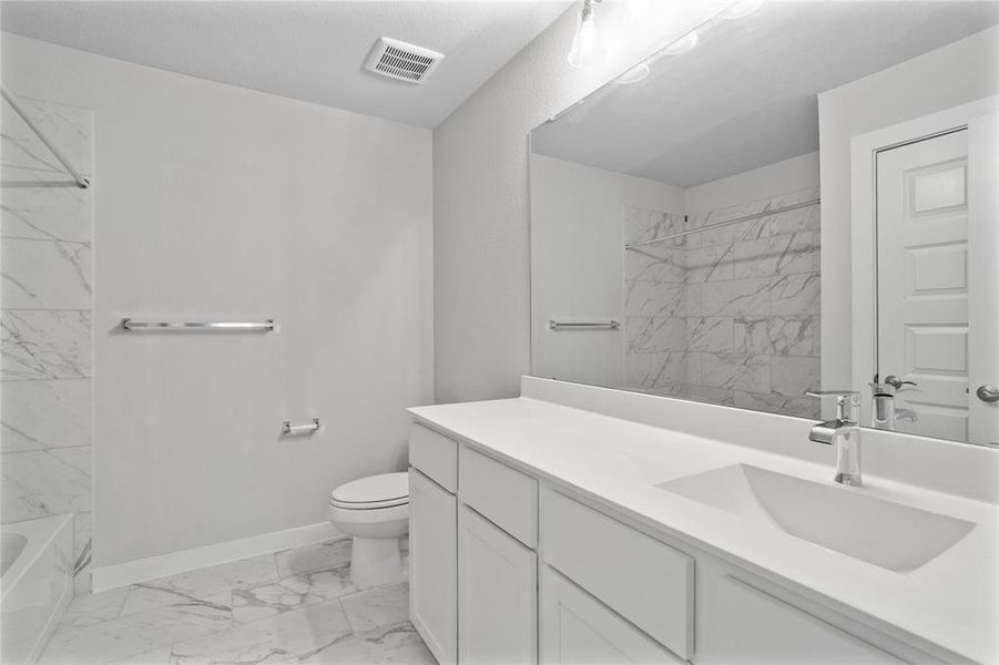 Secondary bath features tile flooring, bath/shower combo with tile surround, white stained wood cabinets, beautiful light countertops, mirror, dark, sleek fixtures and modern finishes.