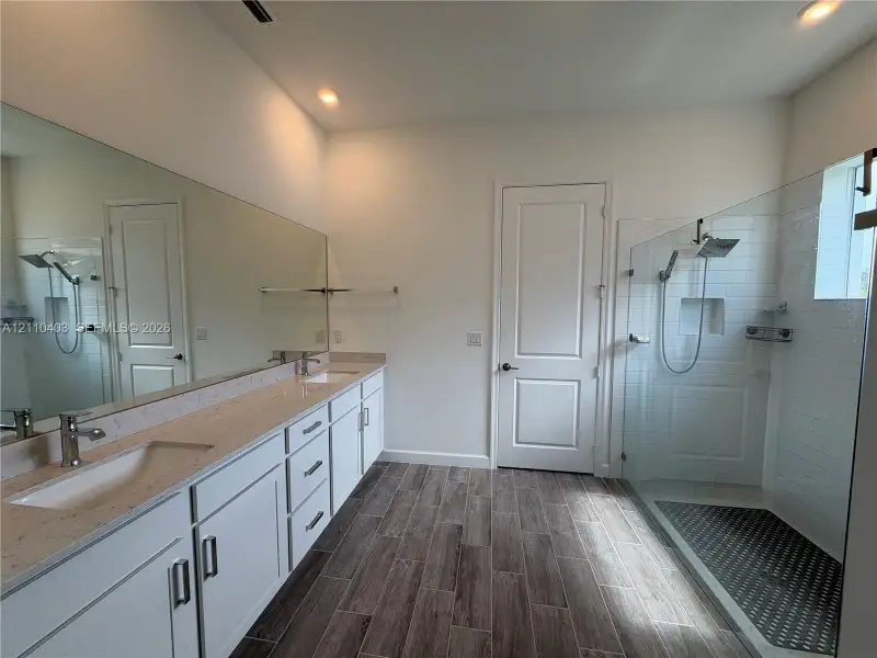 Double vanity featuring white cabinetry, light-toned stone countertops, and a full-width mirror