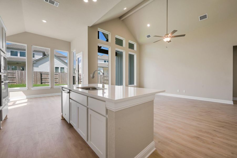Kitchen featuring light wood finished floors, open floor plan, white cabinets, a kitchen island with sink, and beamed ceiling