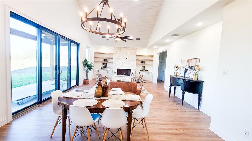 Dining area featuring high vaulted ceiling, an inviting chandelier, light hardwood / wood-style flooring, built in features, and a fireplace