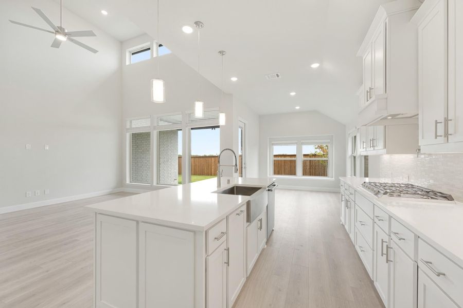 Open kitchen with white cabinets, large island with sink, vaulted ceiling, and light wood floors