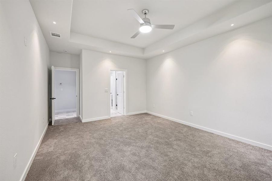 Carpeted empty room with ceiling fan, a tray ceiling, and recessed lighting Carpeted empty room with ceiling fan, a tray ceiling, and recessed lighting