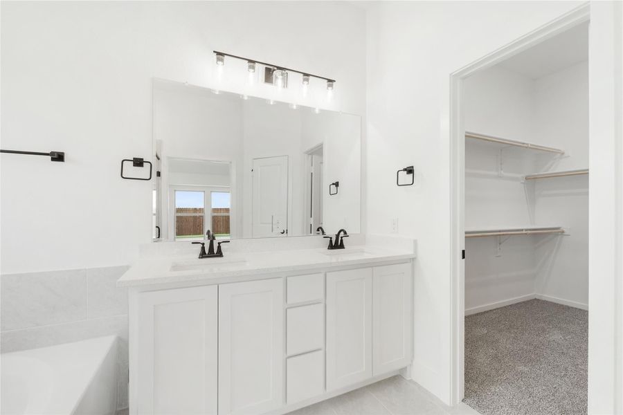 Master bathroom with double sink vanity, white cabinets, large mirror, and walk-in closet entrance