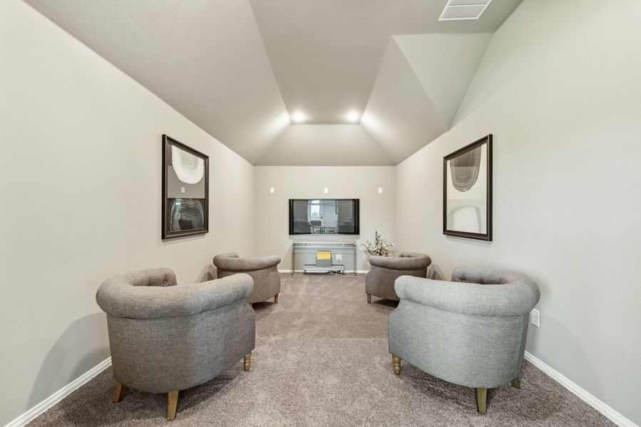 Media room with vaulted ceiling, four gray chairs, wall-mounted TV, and carpet flooring