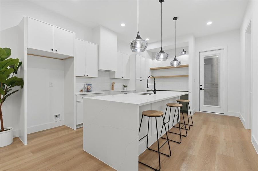 Contemporary kitchen featuring a large waterfall-edge island with seating, white shaker cabinetry, and wood-finish flooring Contemporary kitchen featuring a large waterfall-edge island with seating, white shaker cabinetry, and wood-finish flooring