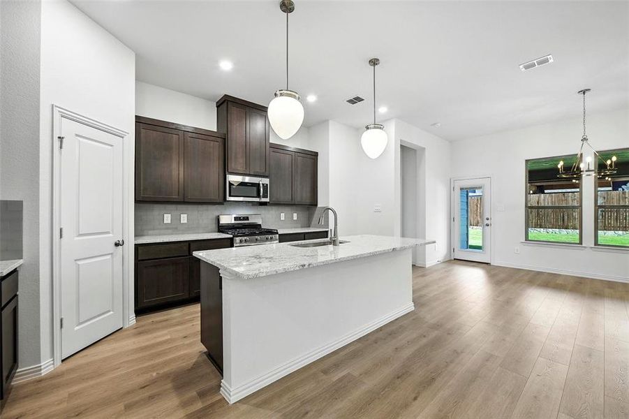 Kitchen featuring appliances with stainless steel finishes, light wood-type flooring, dark brown cabinets, decorative backsplash, and a chandelier