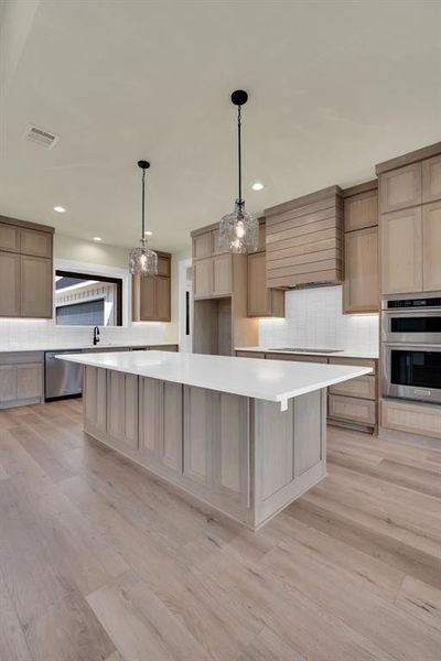 Kitchen with light wood-type flooring, pendant lighting, stainless steel appliances, custom exhaust hood, and decorative backsplash