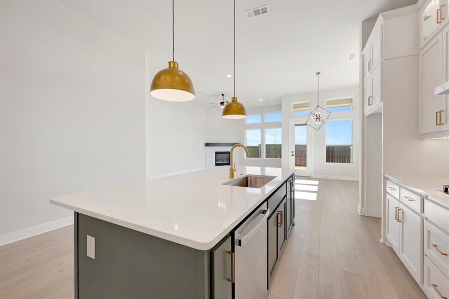 Two tone kitchen with dual tone cabinets, an island with sink, light wood-style flooring, a glass covered fireplace, and stainless steel dishwasher Two tone kitchen with dual tone cabinets, an island with sink, light wood-style flooring, a glass covered fireplace, and stainless steel dishwasher