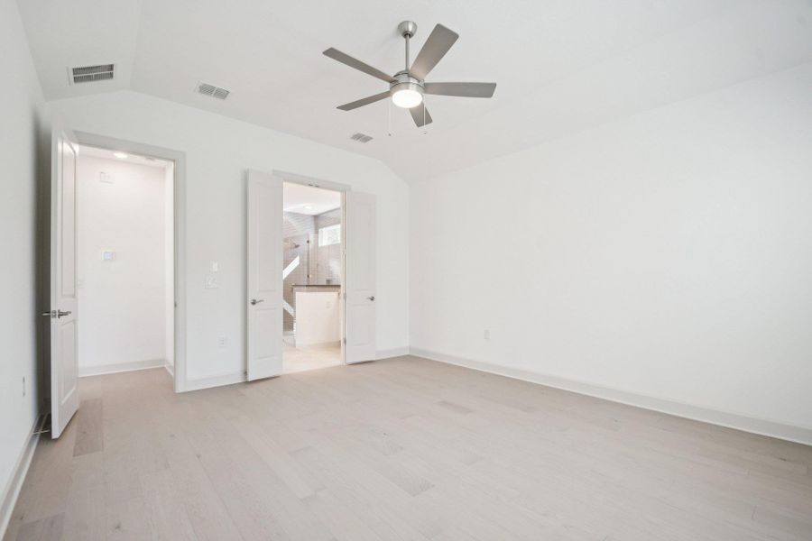 Unfurnished bedroom with light wood-style floors, vaulted ceiling, ceiling fan, and connected bathroom Unfurnished bedroom with light wood-style floors, vaulted ceiling, ceiling fan, and connected bathroom