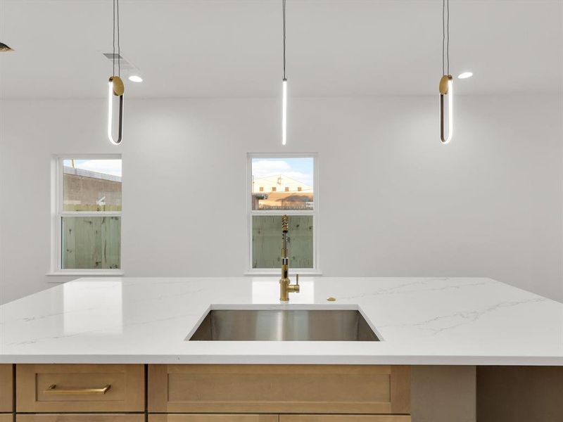 Kitchen featuring light stone counters, sink, and hanging light fixtures