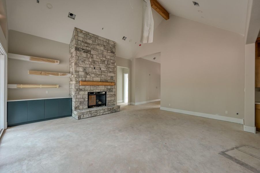 This spacious living room features a high vaulted ceiling and a striking stone fireplace as its centerpiece. There are sleek built-in shelves and cabinets for storage, and the room is filled with natural light from large windows.