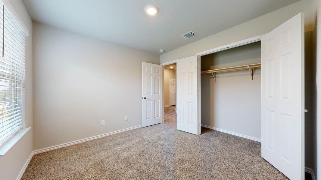 Carpeted room featuring a window with blinds, a bi-fold closet with a wooden rod, and a flush-mount ceiling light