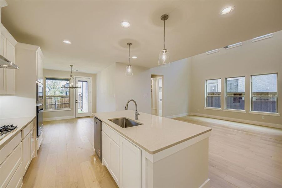 Kitchen with white cabinetry, light wood-style floors, recessed lighting, decorative light fixtures, and a kitchen island with sink Kitchen with white cabinetry, light wood-style floors, recessed lighting, decorative light fixtures, and a kitchen island with sink