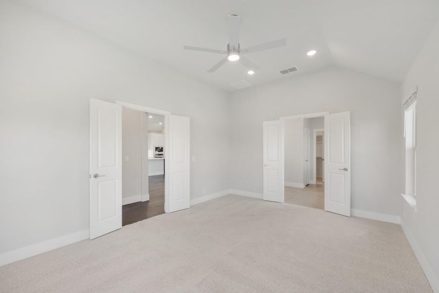 Empty bedroom with carpet, vaulted ceiling, ceiling fan, and two open doorways leading to bathroom and hallway Empty bedroom with carpet, vaulted ceiling, ceiling fan, and two open doorways leading to bathroom and hallway