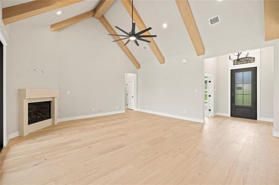 Unfurnished living room featuring a fireplace, beam ceiling, high vaulted ceiling, light wood-type flooring, and recessed lighting Unfurnished living room featuring a fireplace, beam ceiling, high vaulted ceiling, light wood-type flooring, and recessed lighting