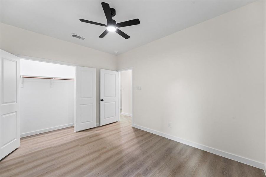 Interior room featuring wood-finish flooring and a black ceiling fan with integrated lighting Interior room featuring wood-finish flooring and a black ceiling fan with integrated lighting