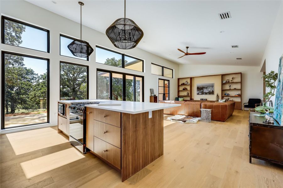 Kitchen featuring light wood finished floors, modern cabinets, hanging light fixtures, stainless steel microwave, and brown cabinetry