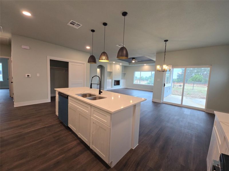Kitchen with ceiling fan, open floor plan, white cabinets, a center island with sink, and decorative light fixtures