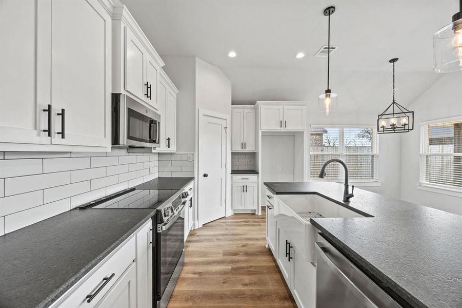 Kitchen with stainless steel appliances, white cabinets, pendant lighting, light wood-type flooring, and decorative backsplash