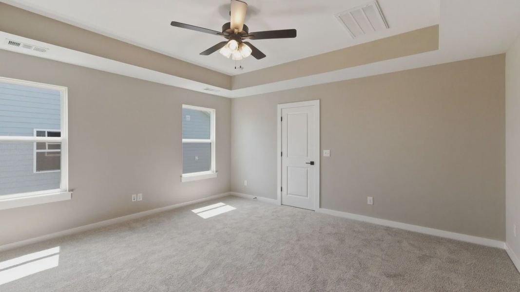 Primary suite with tray ceiling, ceiling fan, and carpet