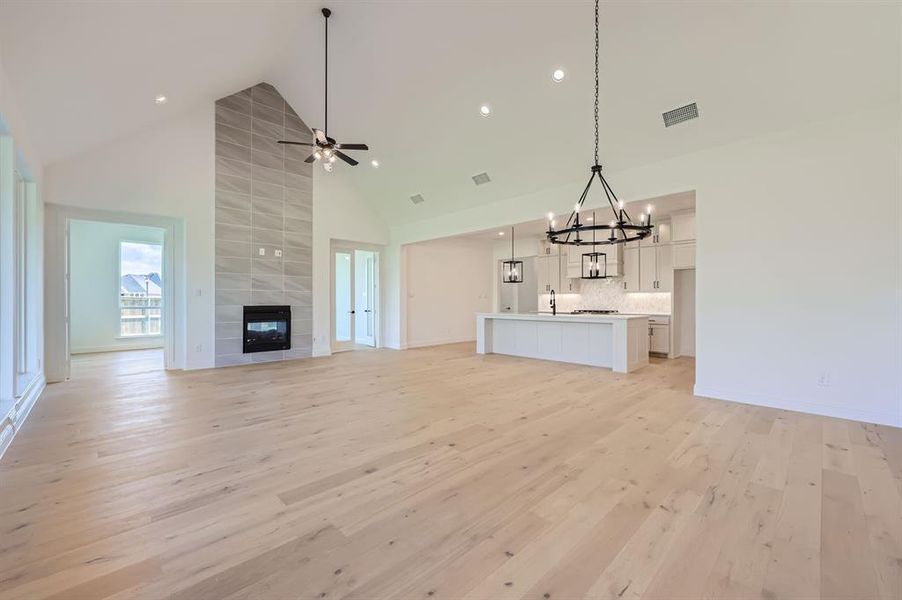 Unfurnished living room with ceiling fan with notable chandelier, high vaulted ceiling, a fireplace, and light hardwood / wood-style flooring