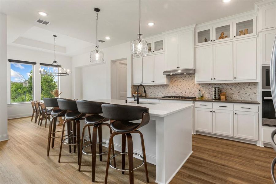 Kitchen featuring under cabinet range hood, a raised ceiling, light wood-type flooring, decorative backsplash, and recessed lighting Kitchen featuring under cabinet range hood, a raised ceiling, light wood-type flooring, decorative backsplash, and recessed lighting