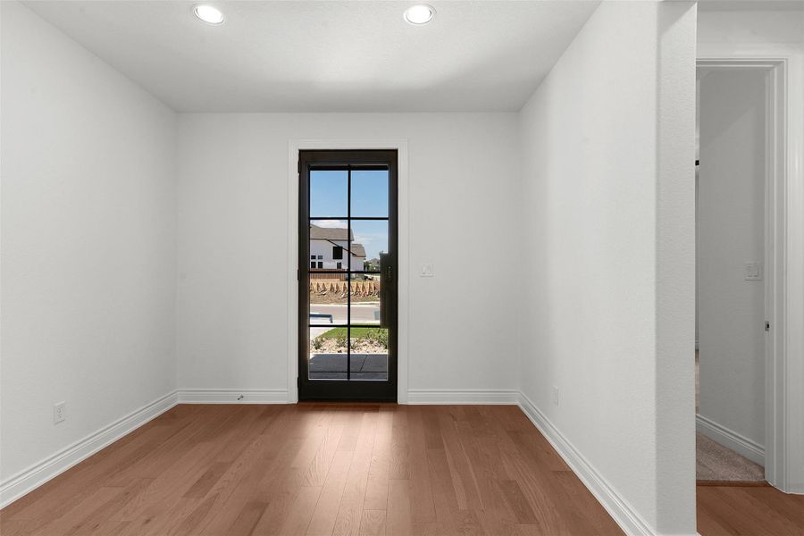 Light-filled room featuring a dark-framed glass-paned door, wood-finish flooring, white baseboards, white walls, and recessed ceiling lighting