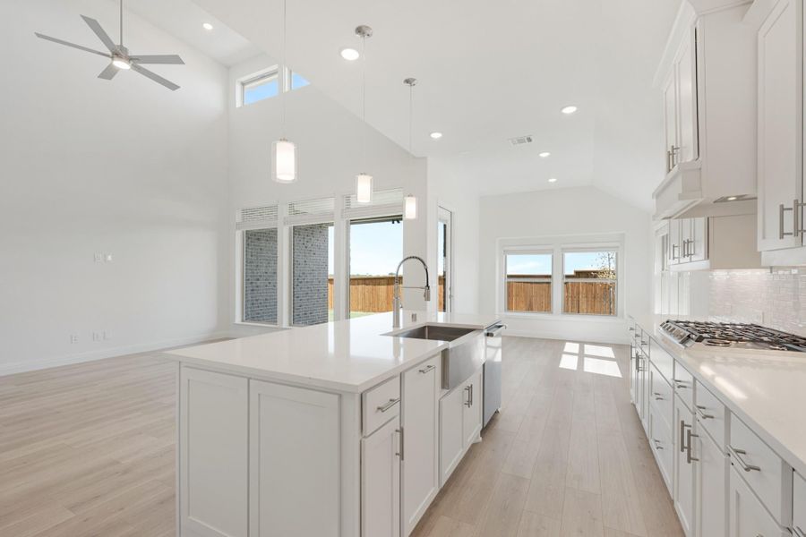 Open kitchen with white cabinets, large island with sink, vaulted ceiling, and light wood floors open to living area Open kitchen with white cabinets, large island with sink, vaulted ceiling, and light wood floors open to living area
