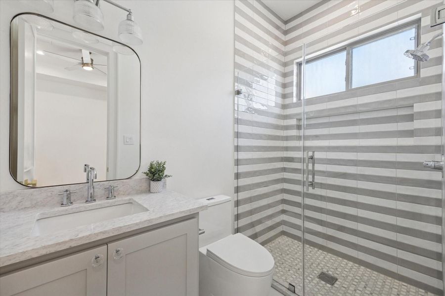 Ensuite bath for the third bedroom features a quartz countertop and Manchester plaid polished marble mosaic tile in the glass enclosed shower.