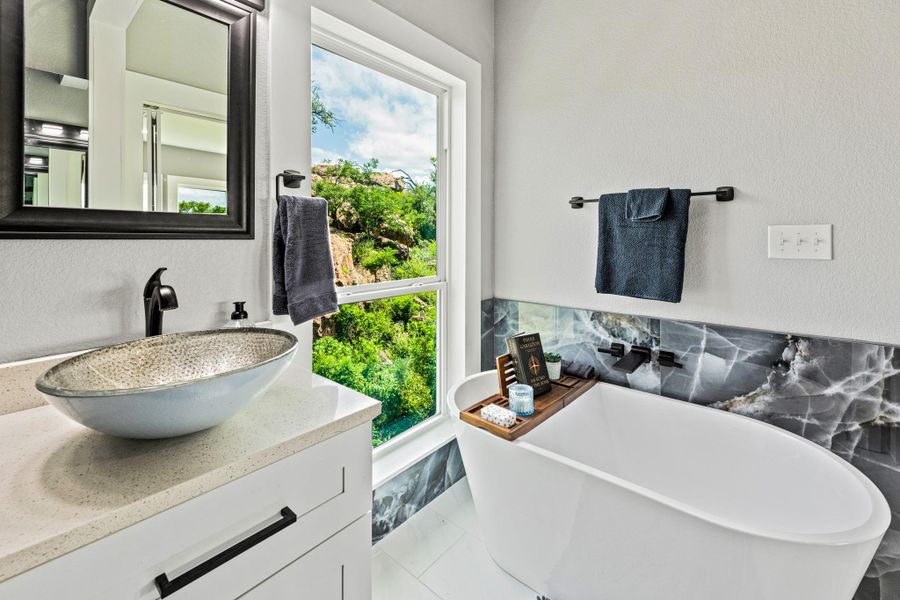Freestanding soaking tub with a dark stone accent wall and wall-mounted faucet